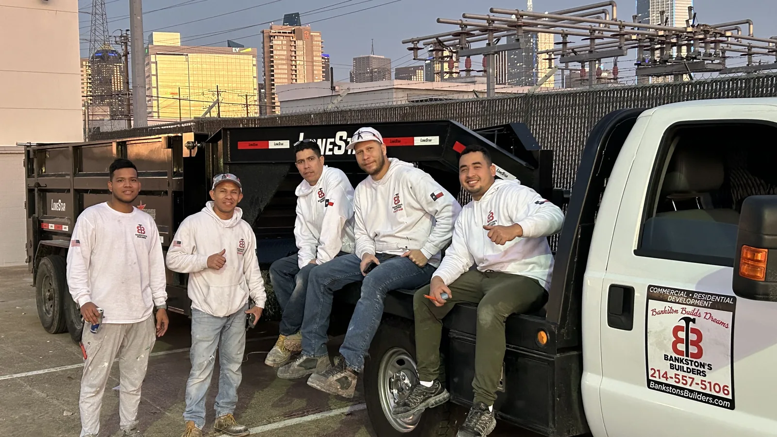 Crew members on a work truck tailgate with a city skyline behind