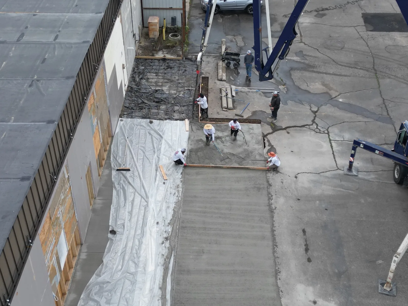 Aerial view of a crew placing a concrete floor pour beside a commercial building with a pump boom, commercial new construction