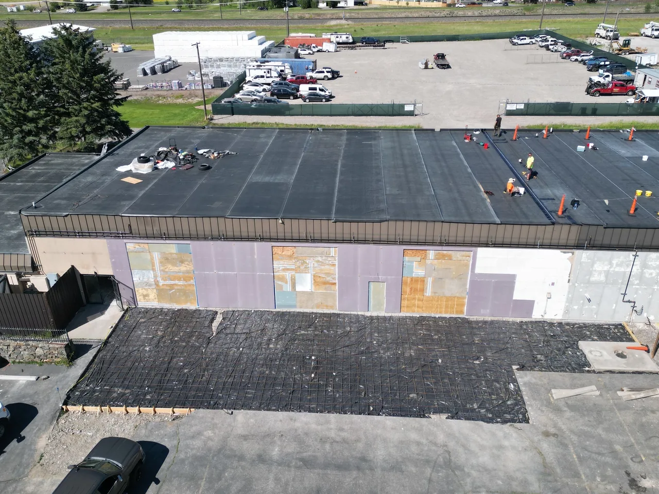 Aerial view of crews installing a new membrane roof on a commercial building expansion, commercial new construction