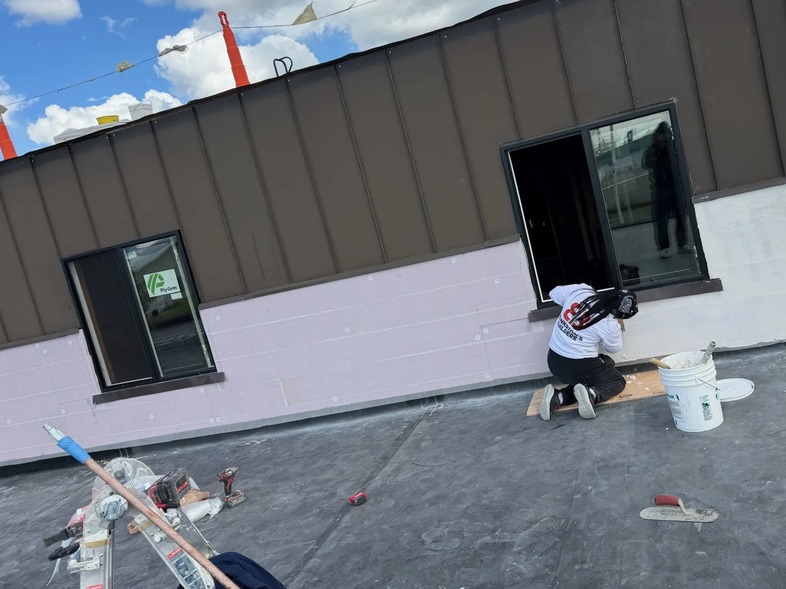 Crew member sealing a new window in a rebuilt upper wall on a commercial building roof, commercial new construction