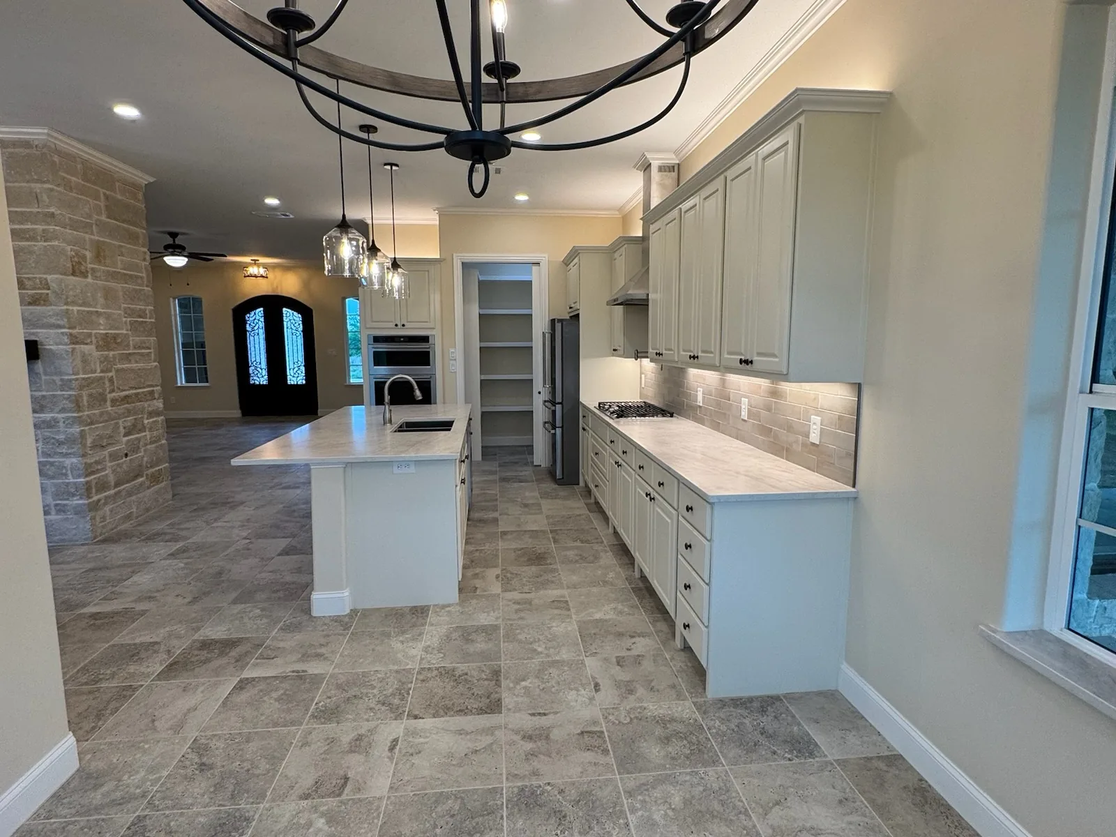 New kitchen with an island, a stone column and arched iron entry doors, custom home construction