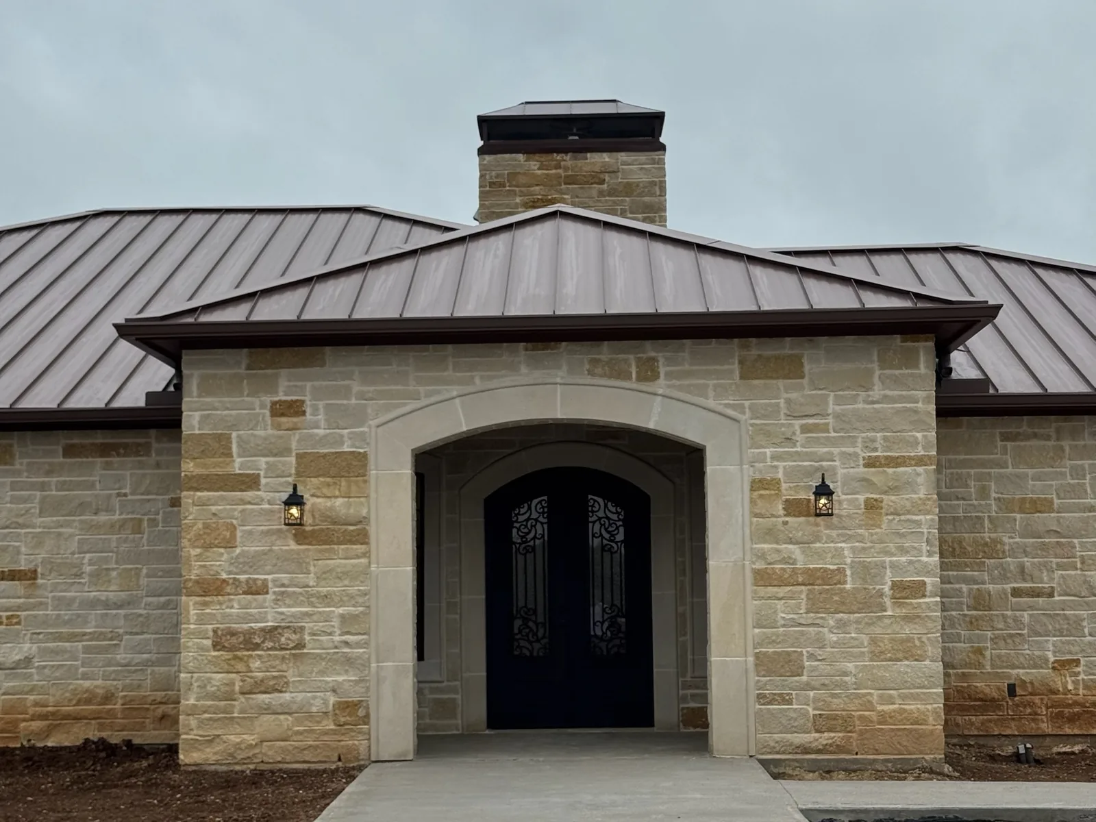 New stone home with an arched entry, an iron front door and a standing seam roof, custom home construction
