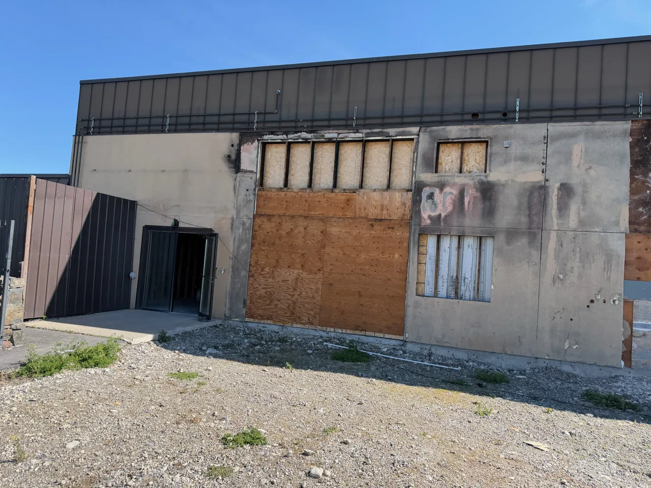 Fire damaged building wall with charred siding and boarded up openings, fire and water damage repair