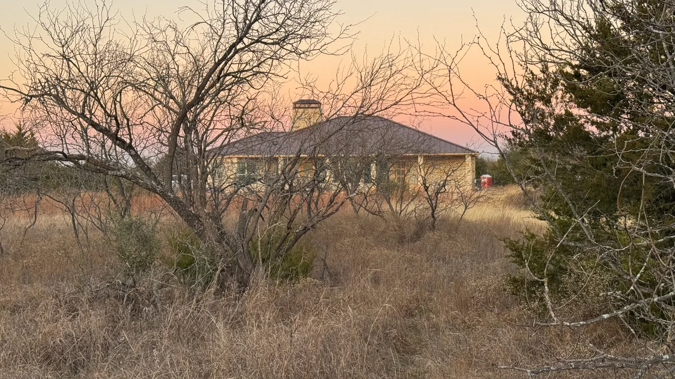 Stone ranch house behind winter brush at sunset in North Texas