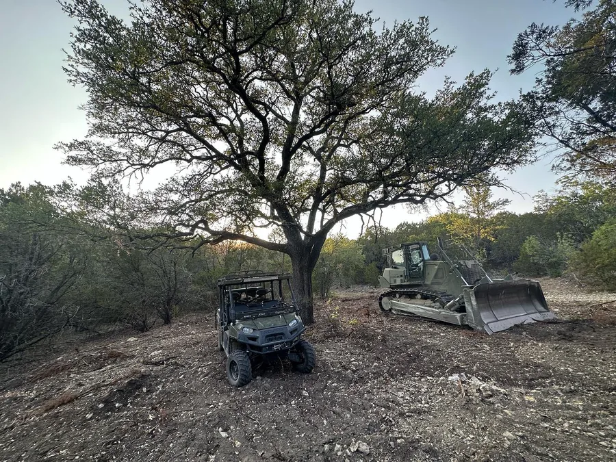 Dozer and utility vehicle in cleared brush under a live oak, land clearing