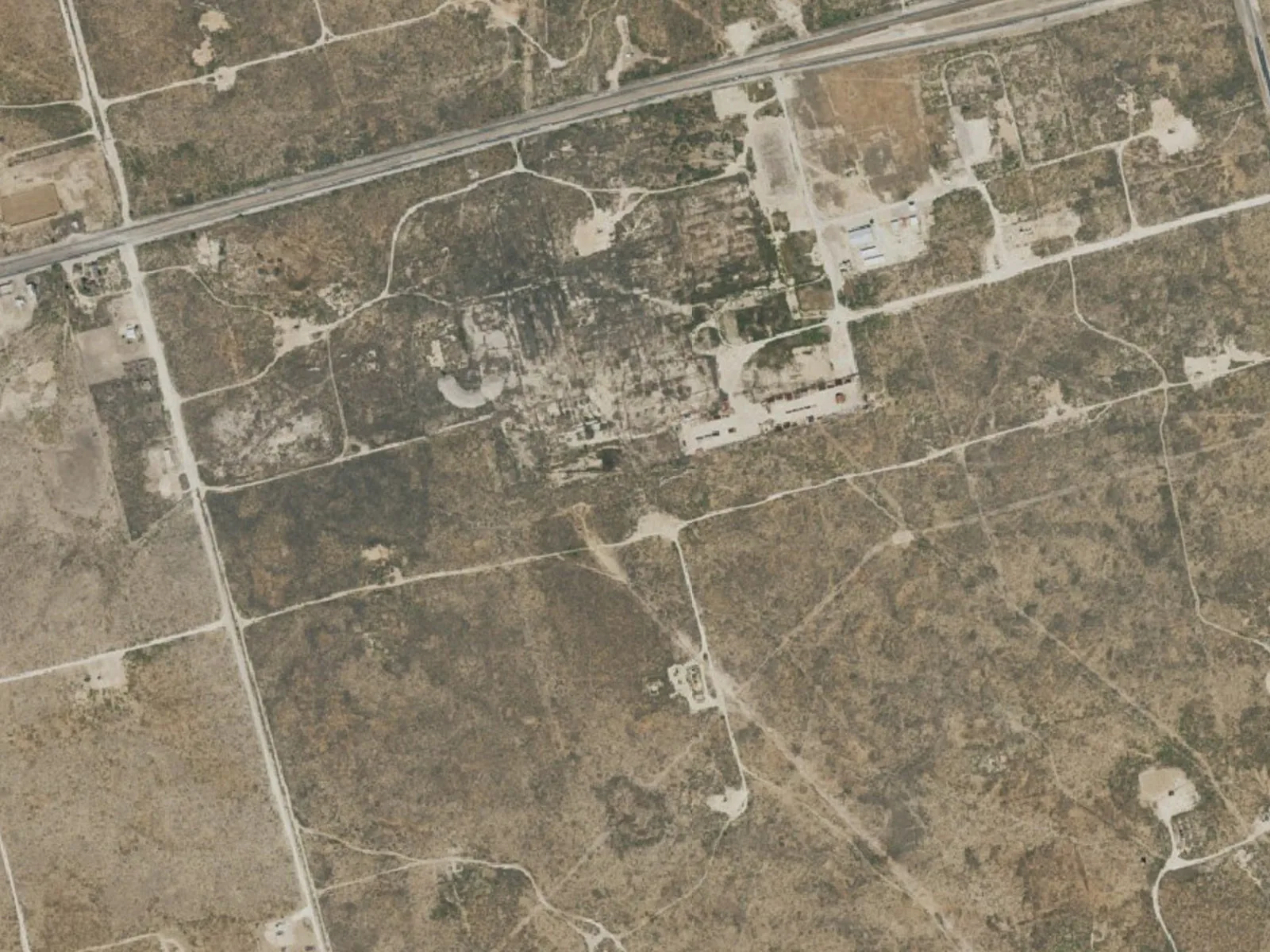 Aerial view of oil well pads and lease roads across flat treeless ranch land, oilfield construction
