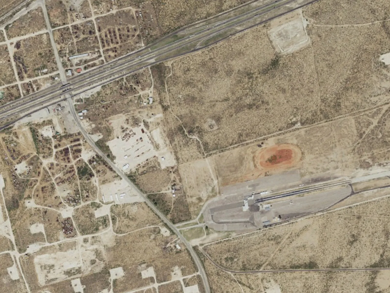 Aerial view of well pads, lease roads and a highway on flat land, oilfield construction