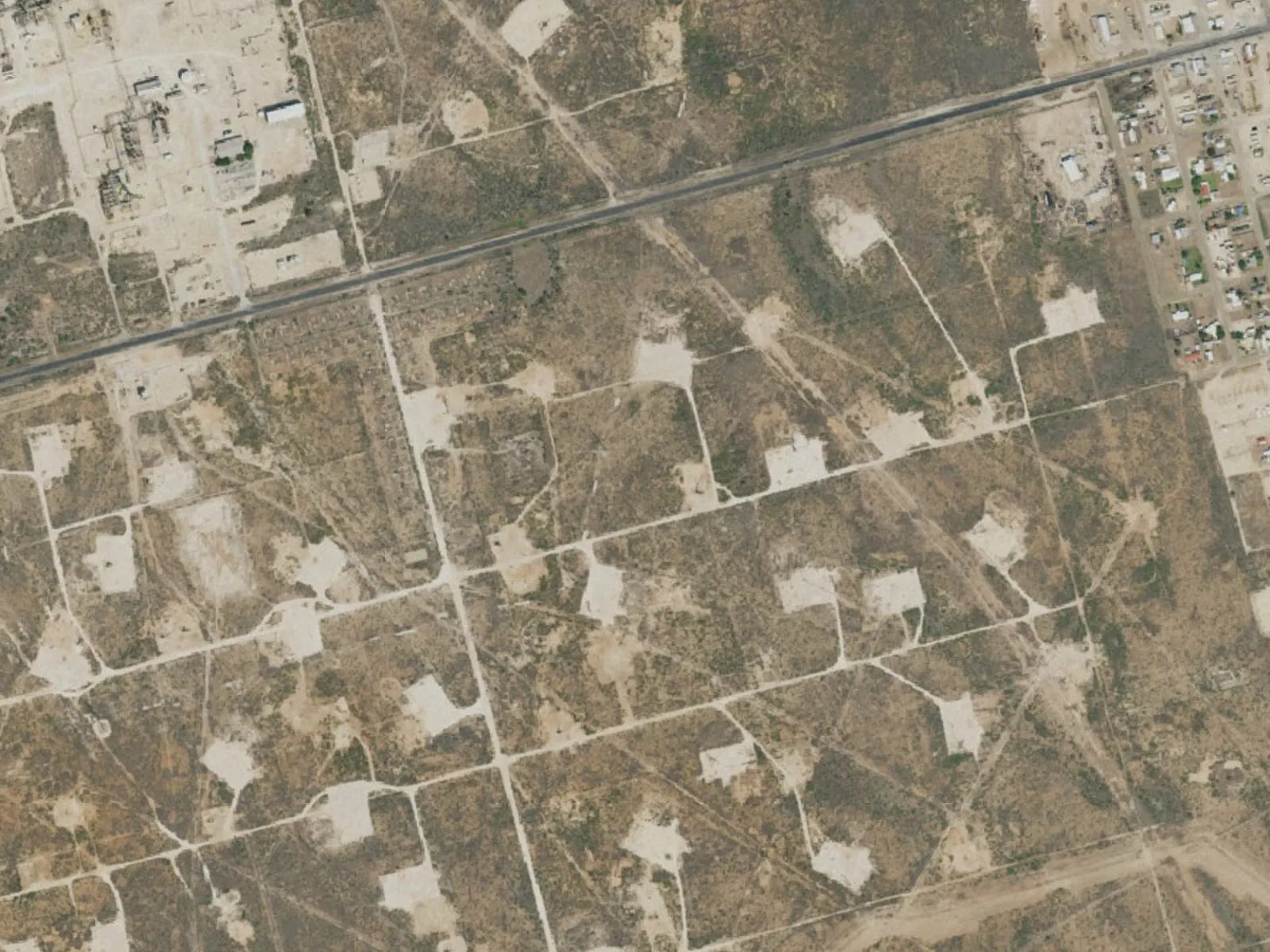 Aerial view of well pads and lease roads on flat West Texas land, oilfield construction