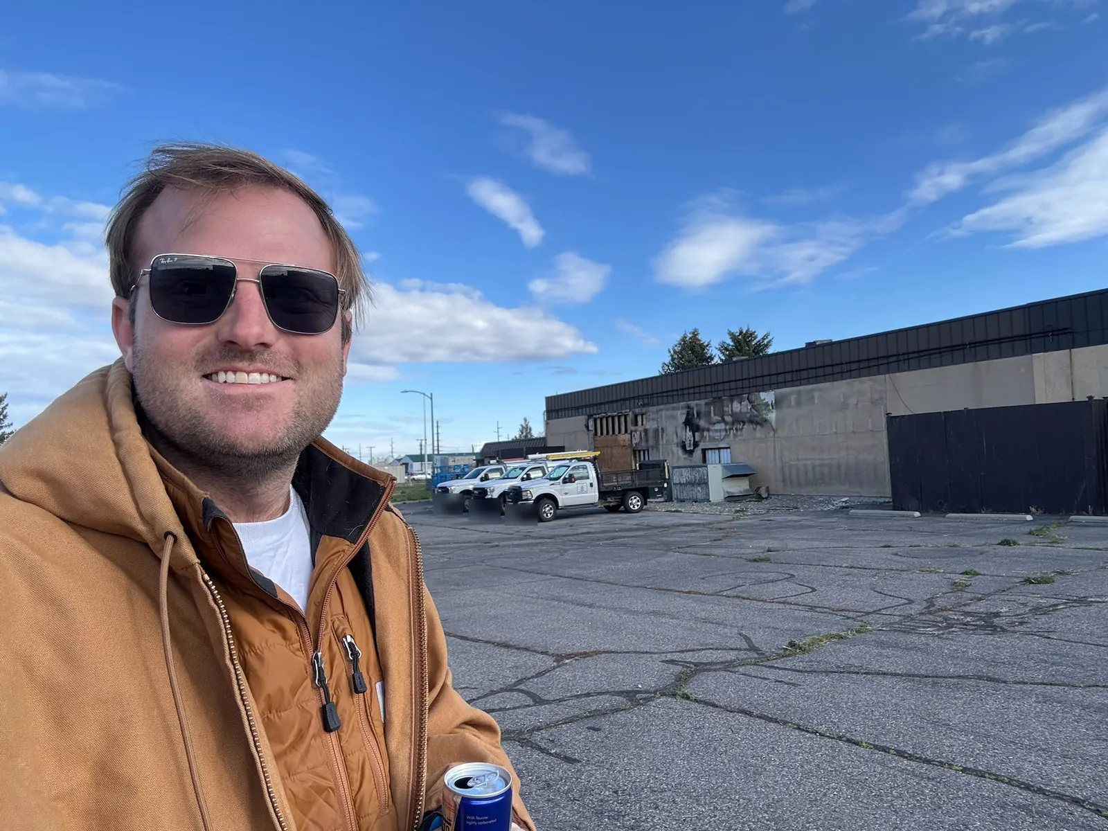 Selfie in front of a fire damaged building with charred siding and boarded openings, commercial construction