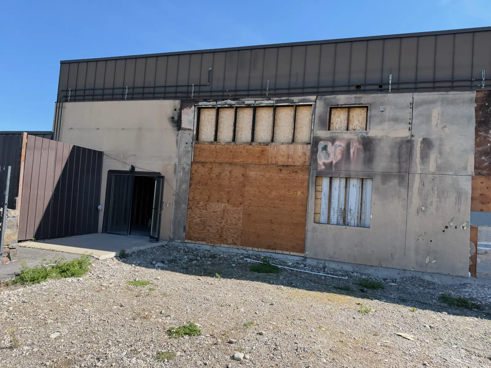 Fire damaged wall with charred siding and boarded up openings, commercial construction