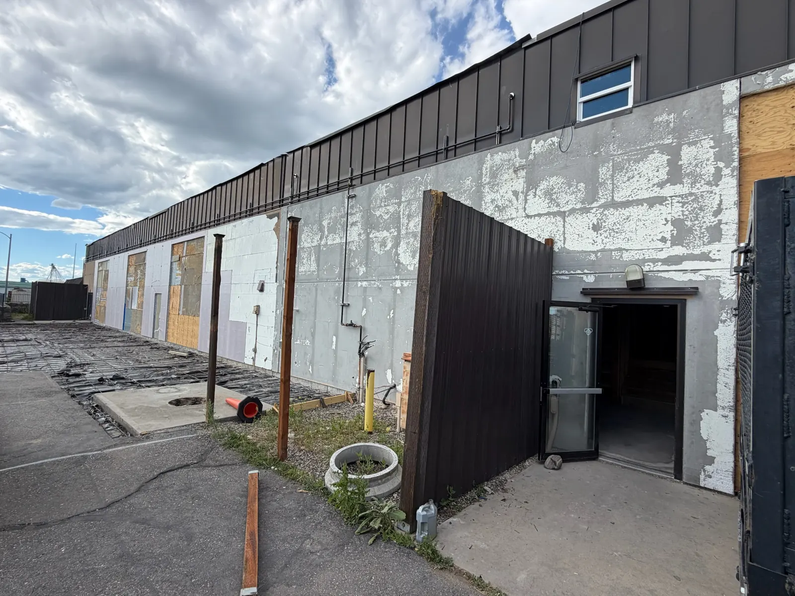 Exterior wall with peeling paint, patched siding and rebar set for a new apron, commercial construction