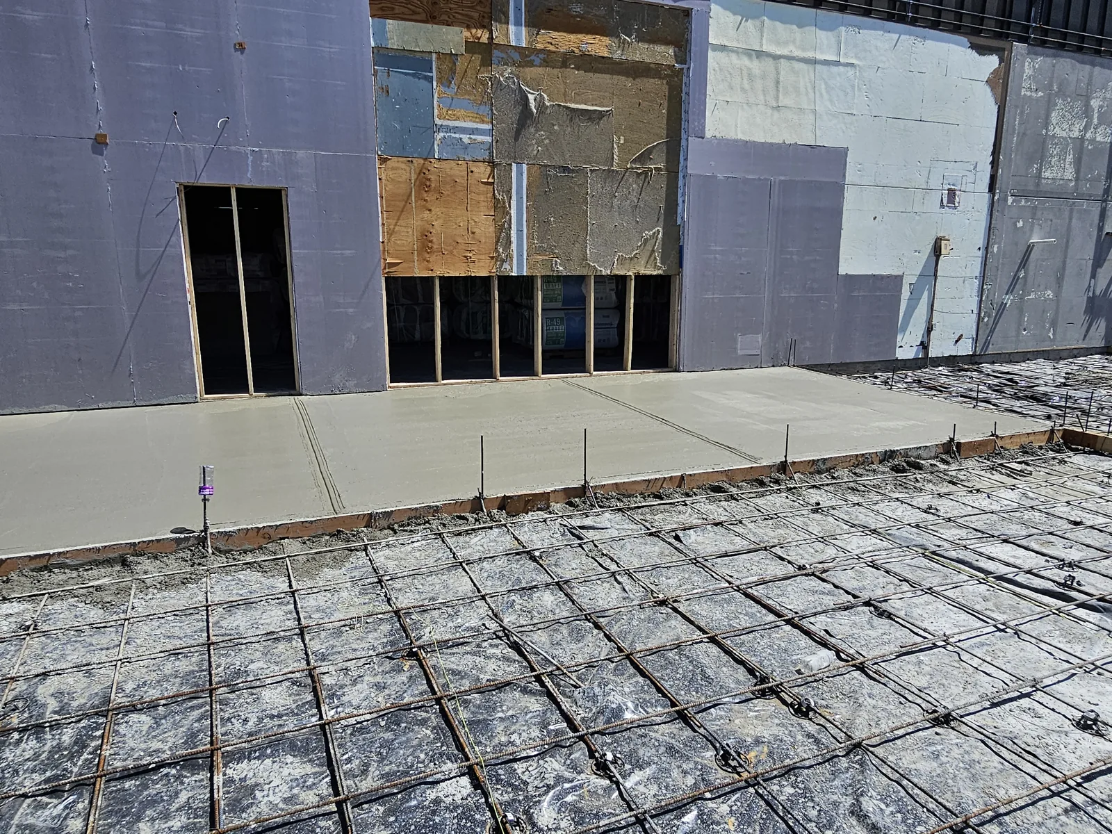 New concrete floor pour along the building with rebar set for the next pour, commercial construction