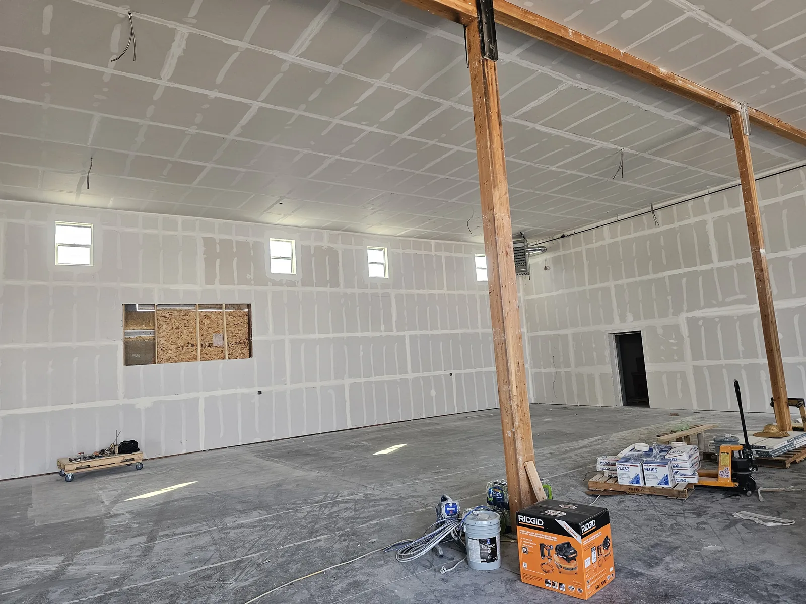Taped drywall in a large warehouse bay with timber posts, commercial construction