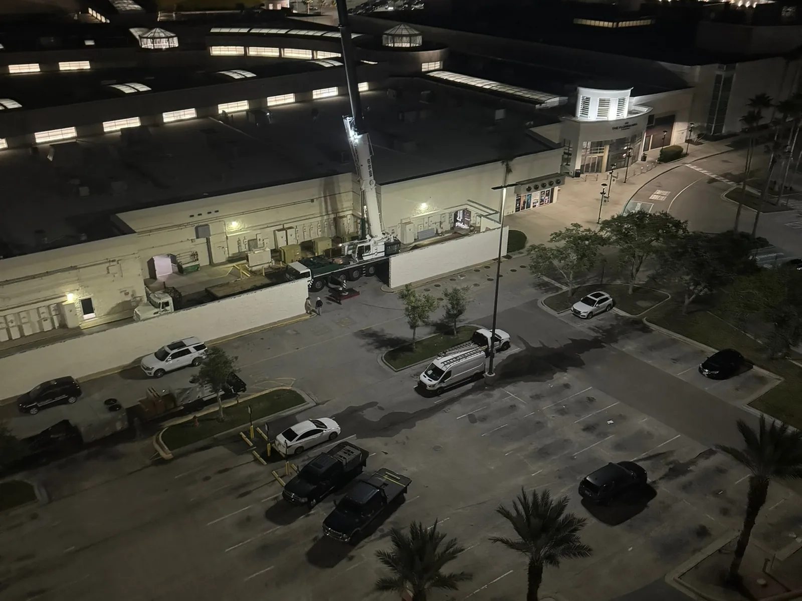 Crane at the back of a mall at night with palm trees in the lot, commercial construction