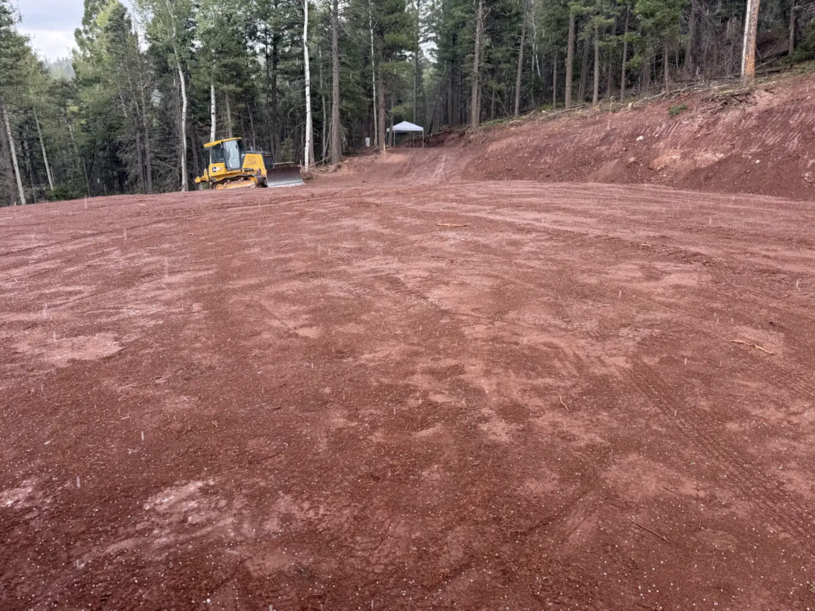 Freshly graded building pad with a dozer at its edge below a cut slope, site preparation