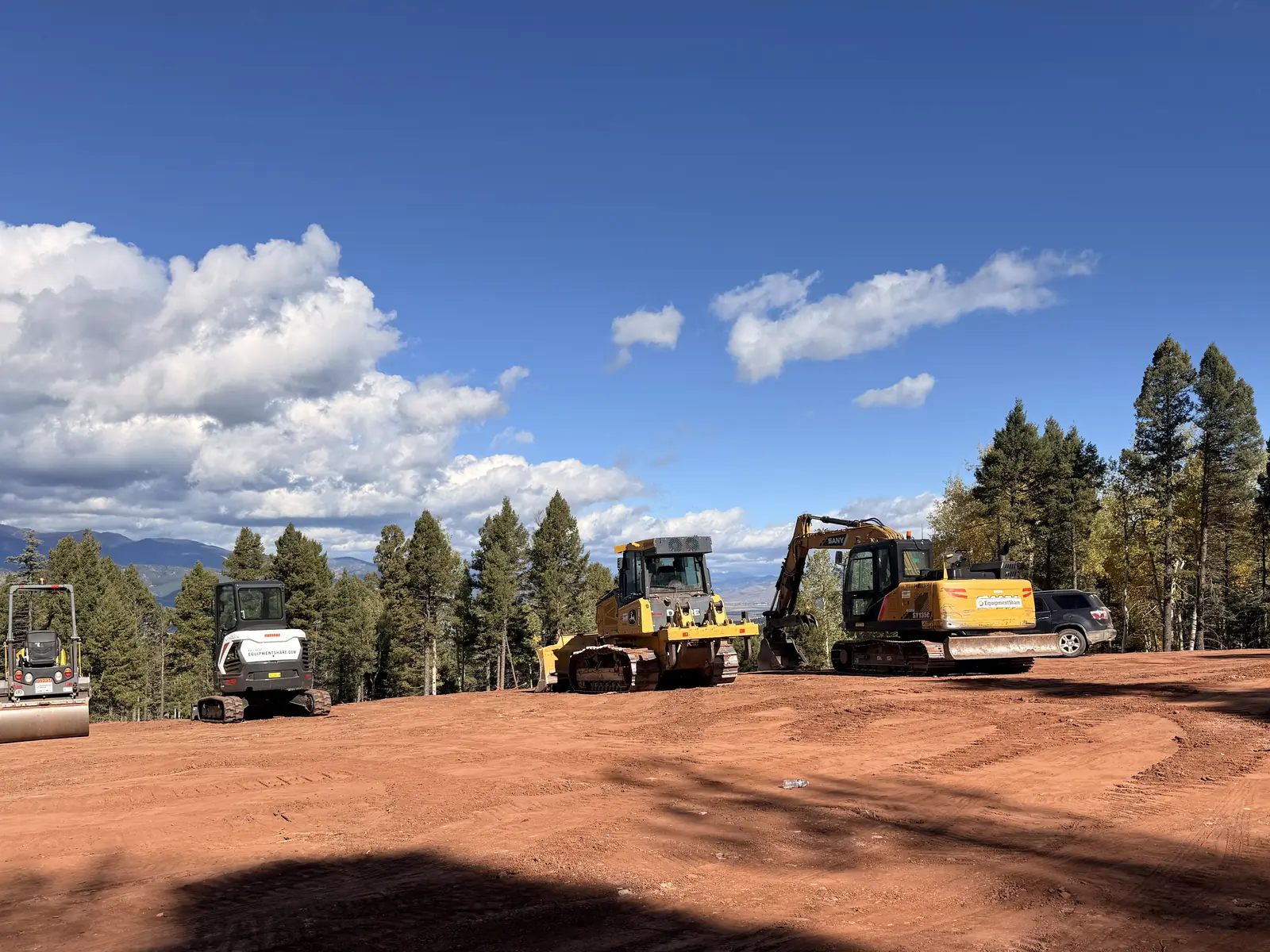 Roller, mini excavator, dozer and excavator lined up on a graded pad, site preparation