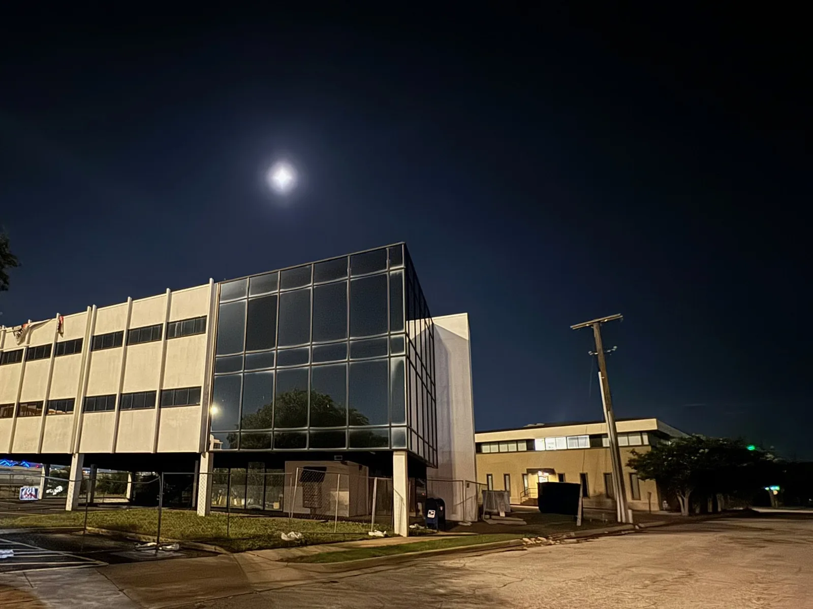 Vacant three story office building behind construction fencing at night, commercial construction