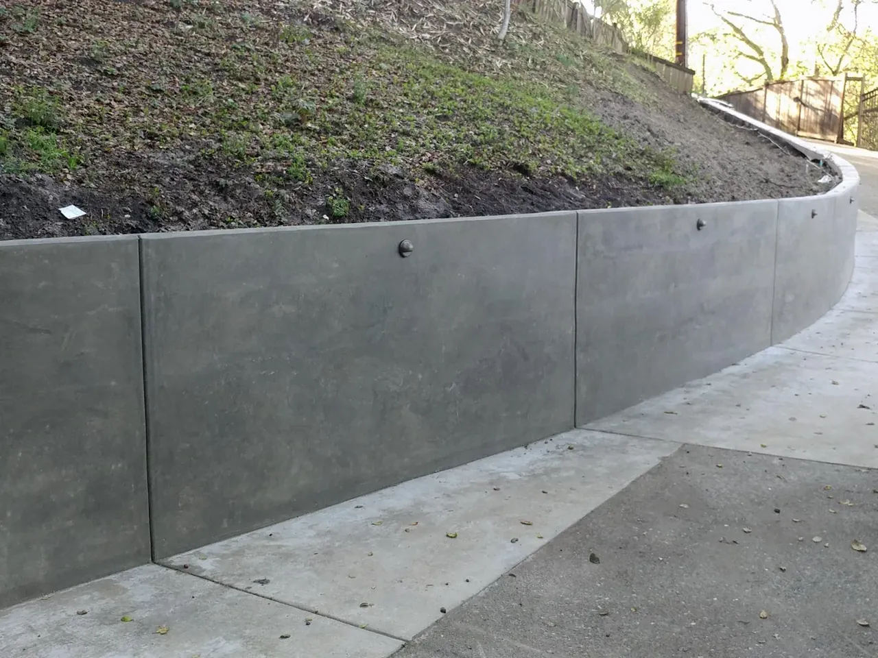 Poured concrete retaining wall along a concrete drive below a slope, retaining walls