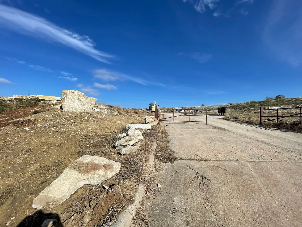 Access road with a gate and limestone boulders along a cleared lot, road building