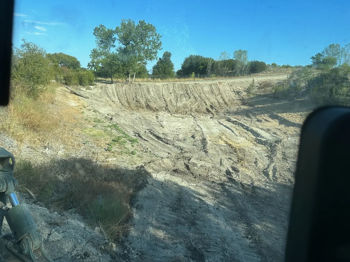 Graded drainage basin cut into a slope, seen from the machine cab, site drainage