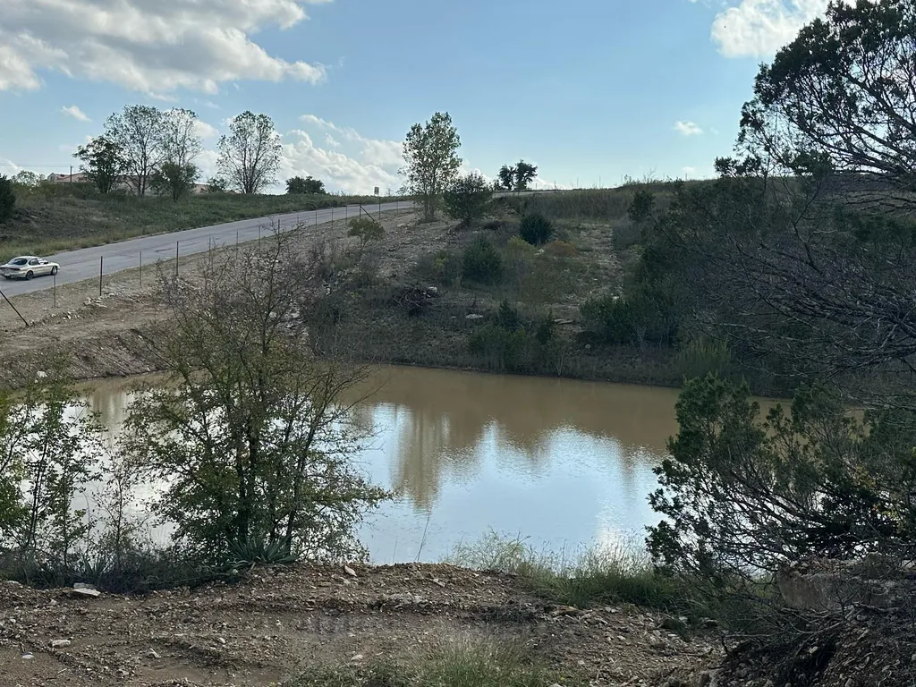 Stock tank held by an earthen dam on ranch land, site drainage