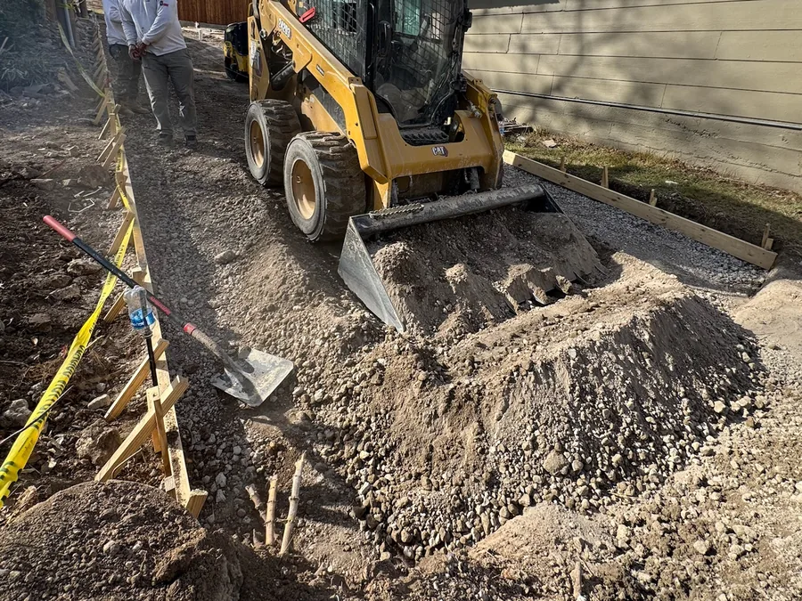 Skid steer spreading gravel base beside a house, site preparation