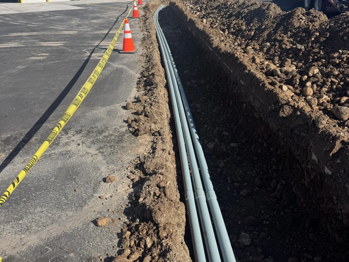 Open trench with electrical conduit laid beside a new paved lot, utility trenching
