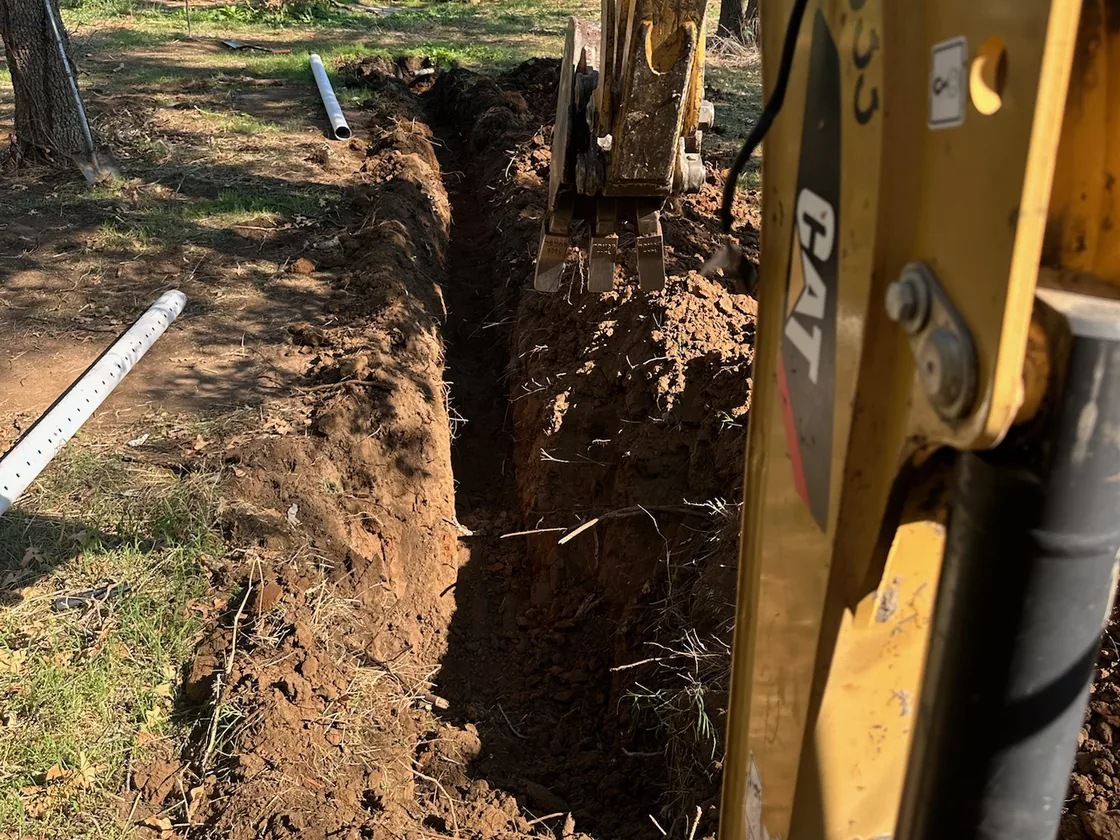 Excavator bucket digging a narrow pipe trench, utility trenching