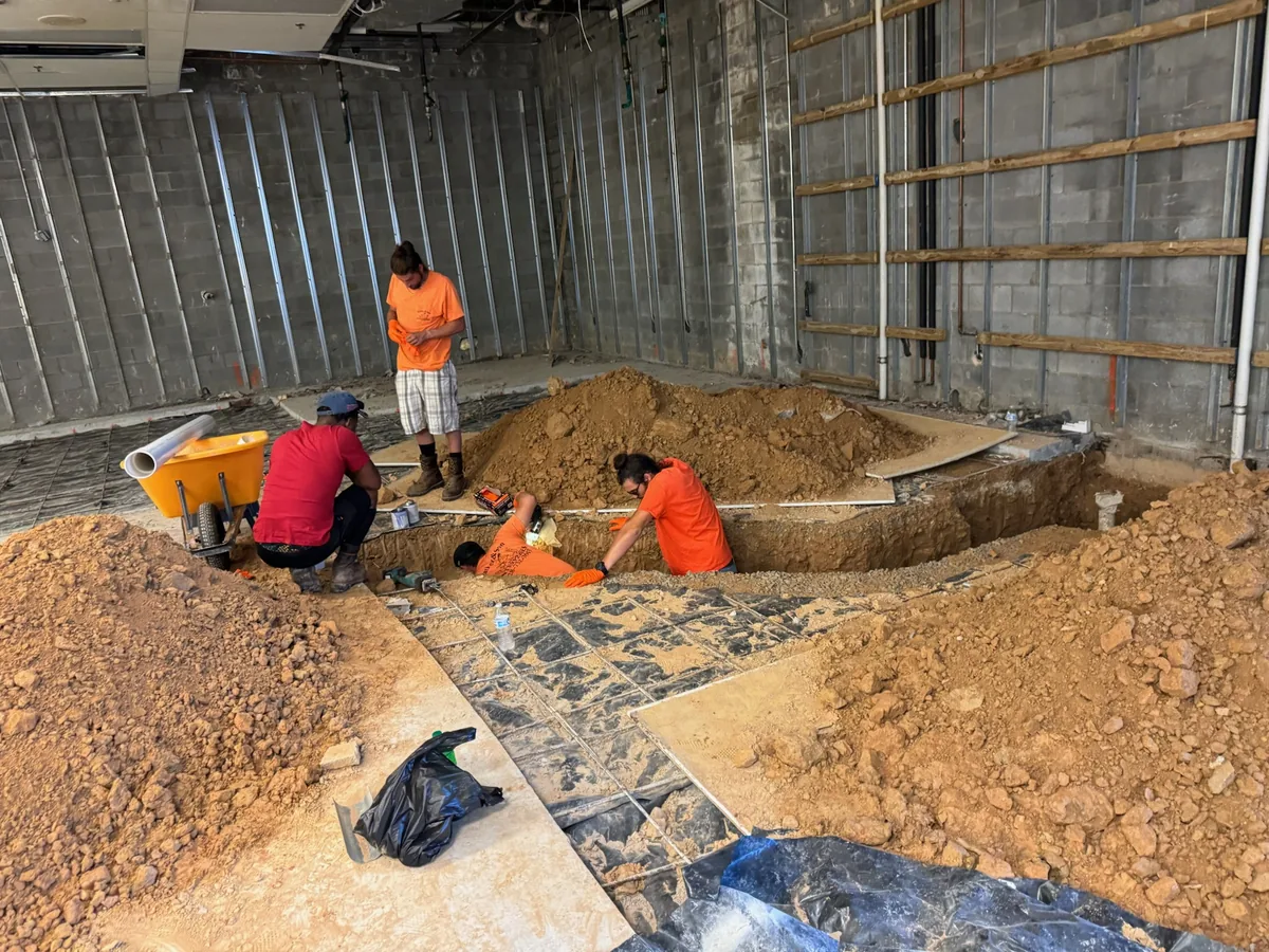 Crew digging a pipe trench through the floor of a commercial building, utility trenching